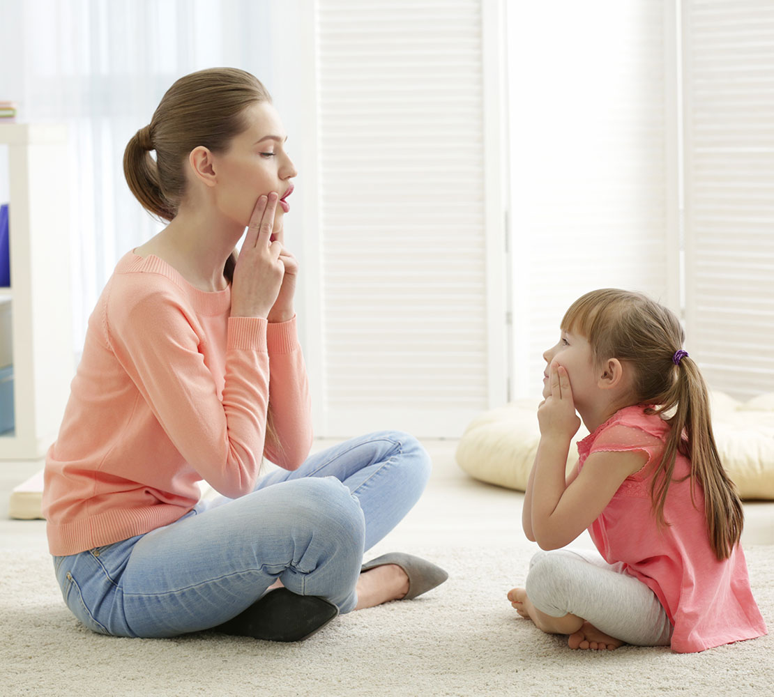 A female Speech Language pathologist is training a small girl to improve verbal communication.