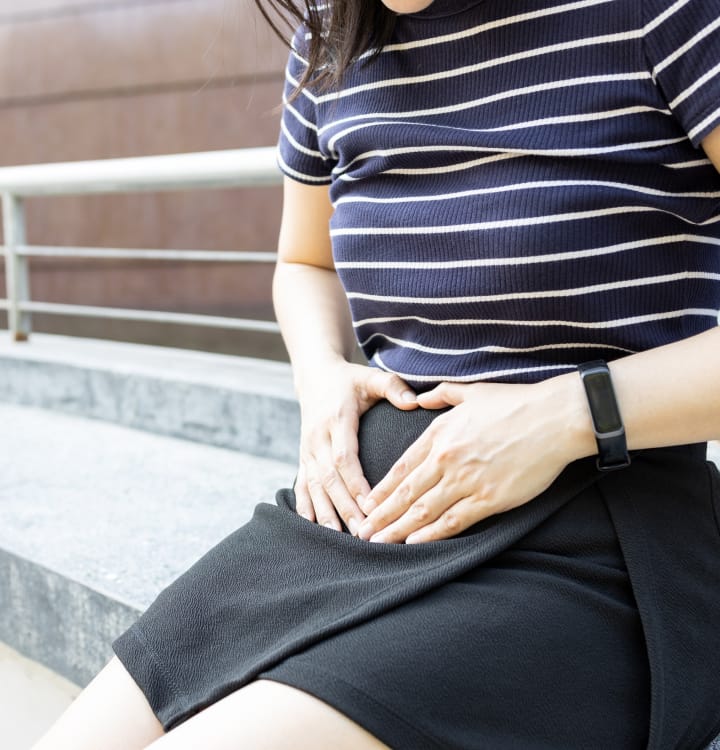 A woman sitting with both hands gently placed on her abdomen.