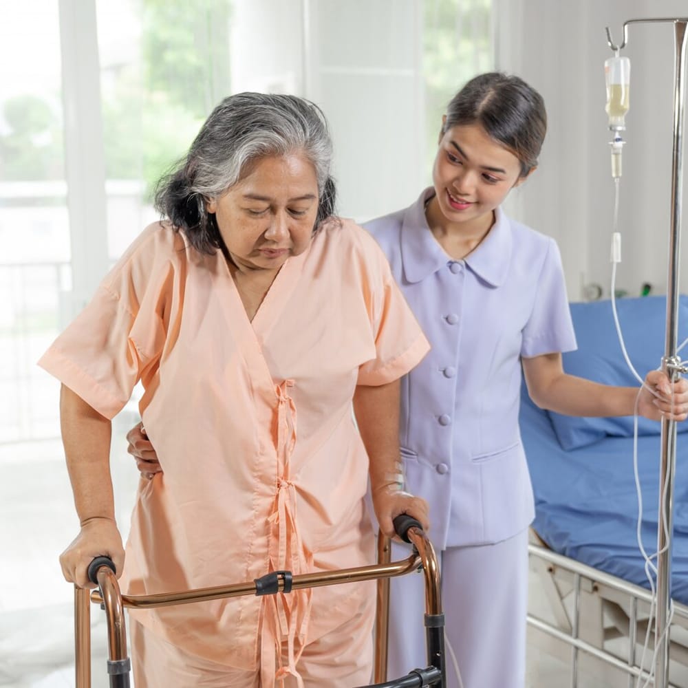 An elderly woman using a walker, being assisted by a healthcare worker.
