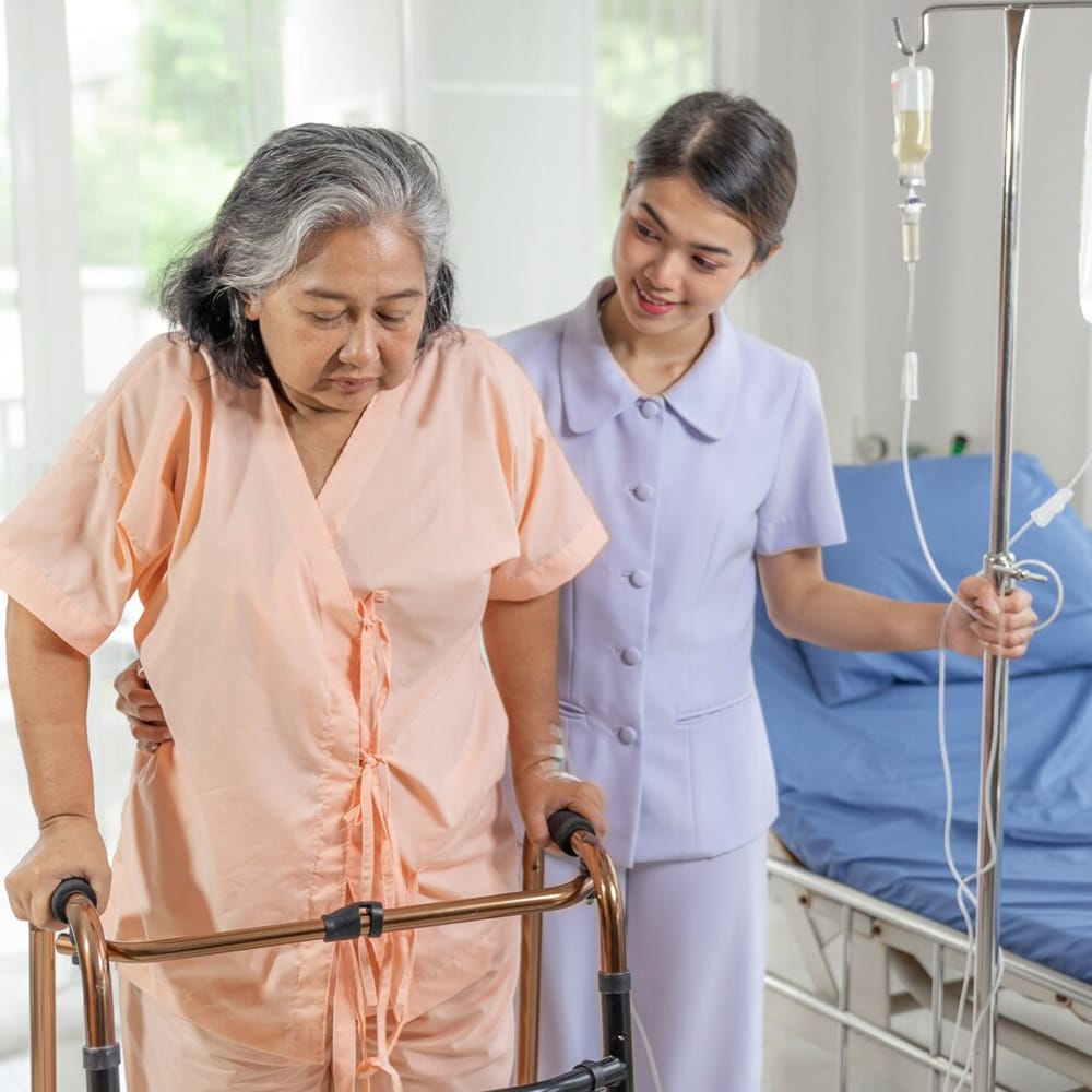 An elderly woman using a walker, being assisted by a healthcare worker.